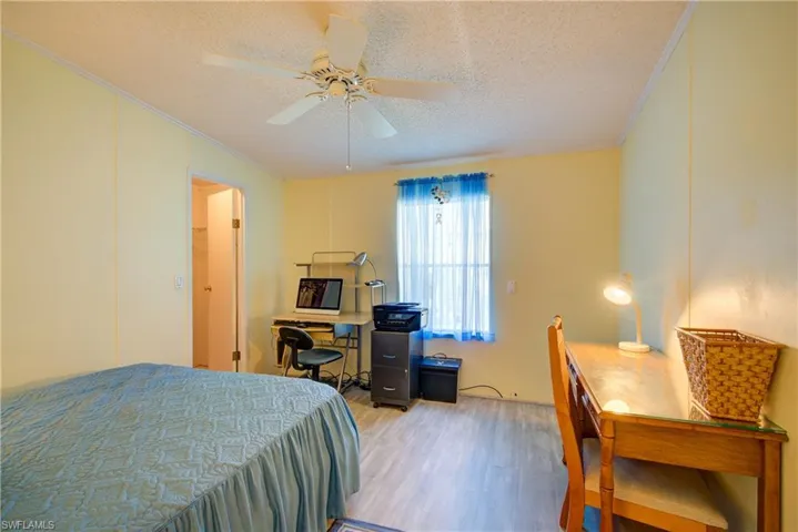 Bedroom with crown molding, wood finished floors, a textured ceiling, an office area, and a ceiling fan
