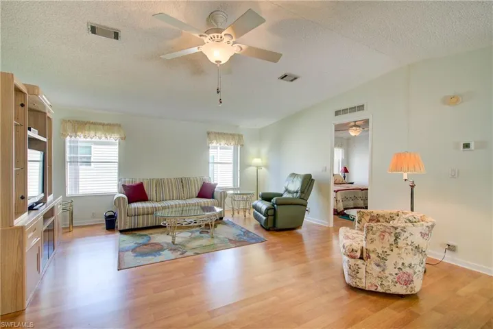 Living room with a ceiling fan, a textured ceiling, light wood-type flooring, and lofted ceiling