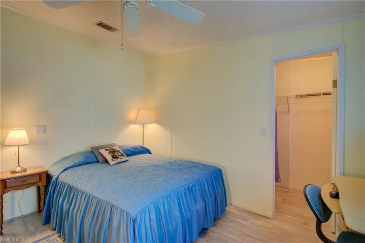 Bedroom featuring wood finished floors, a textured ceiling, ceiling fan, a spacious closet, and crown molding