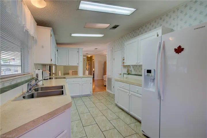 Kitchen with white refrigerator with ice dispenser, white cabinets, decorative backsplash, light countertops, and a textured ceiling