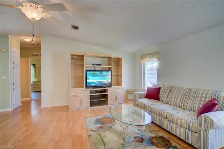 Living area with light wood-style floors, lofted ceiling, a textured ceiling, and a ceiling fan