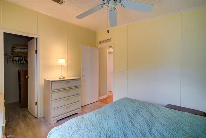 Bedroom featuring a textured ceiling, light wood-style flooring, a spacious closet, a decorative wall, and ceiling fan