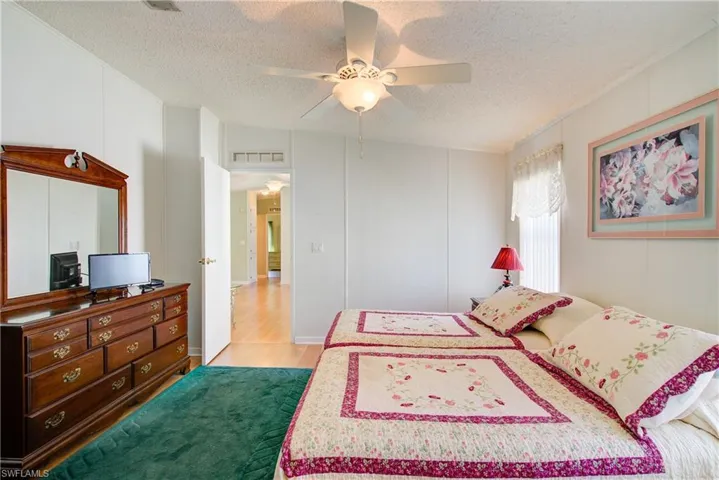 Bedroom featuring light wood-style floors, ceiling fan, a textured ceiling, and a decorative wall