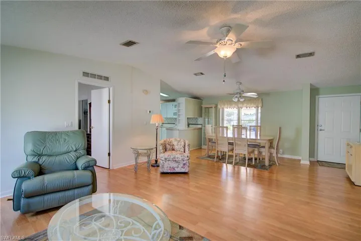 Living area featuring light wood-style flooring, a textured ceiling, lofted ceiling, and ceiling fan