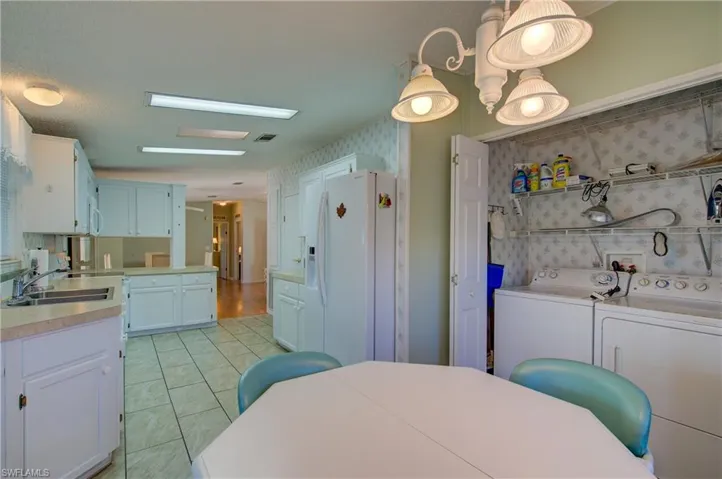 Kitchen with white appliances, white cabinetry, light countertops, light tile patterned floors, and washing machine and dryer