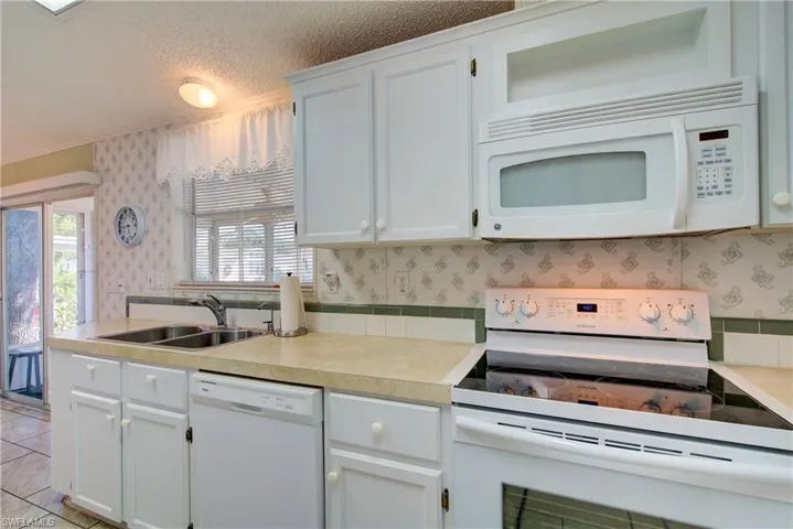 Kitchen with white appliances, wallpapered walls, light countertops, white cabinetry, and a textured ceiling