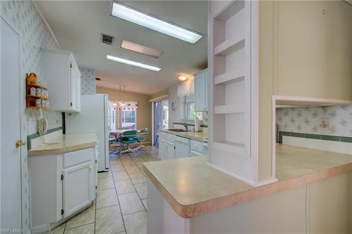 Kitchen featuring open shelves, white cabinets, wallpapered walls, light countertops, and tasteful backsplash