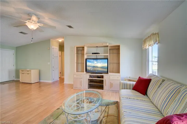 Living room with light wood finished floors, a textured ceiling, lofted ceiling, and a ceiling fan