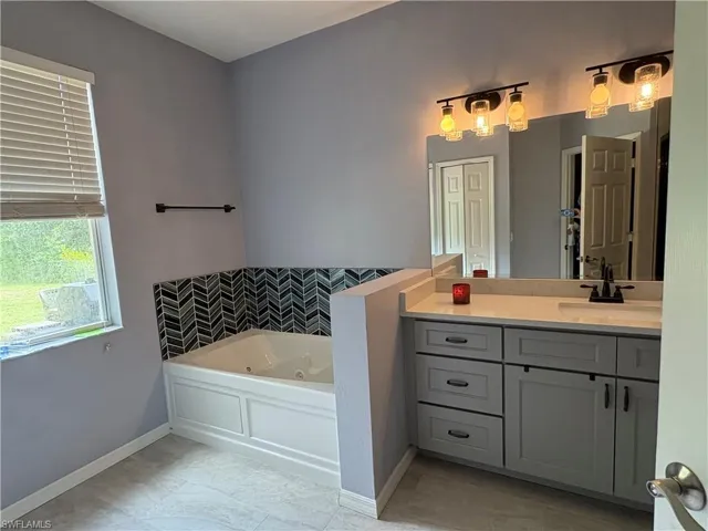 Full bath featuring a jetted tub, vanity, and tile patterned flooring