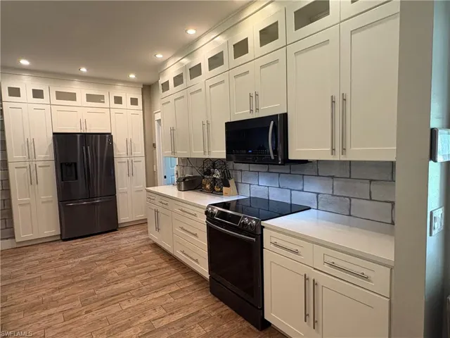 Kitchen with stainless steel fridge, range with electric stovetop, black microwave, white cabinets, and wood finished floors