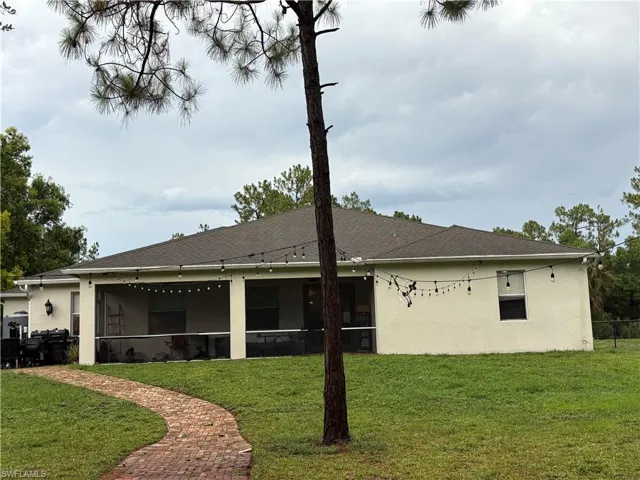 Rear view of property with a sunroom, stucco siding, and roof with shingles