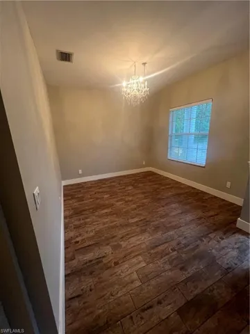 Unfurnished room with a chandelier and dark wood finished floors