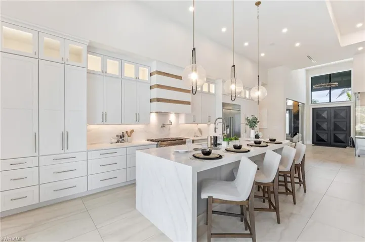 Kitchen featuring a towering ceiling, a large island, high end refrigerator, light tile patterned floors, and glass insert cabinets