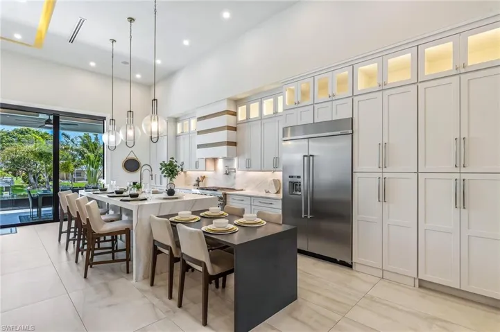 Kitchen with premium appliances, a center island with sink, custom exhaust hood, a kitchen breakfast bar, and decorative light fixtures