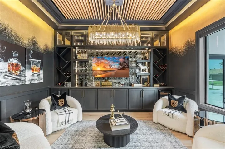 Indoor bar with wood finished floors, a tray ceiling, a chandelier, and crown molding