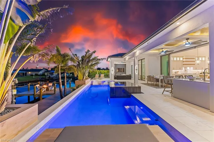 Pool at dusk featuring a bar, an outdoor kitchen, a ceiling fan, an outdoor pool, and a patio area