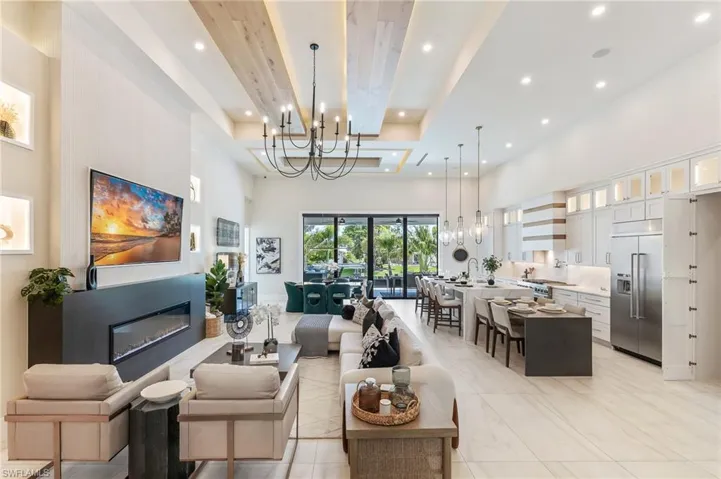 Living area with a high ceiling, a chandelier, recessed lighting, a raised ceiling, and a glass covered fireplace