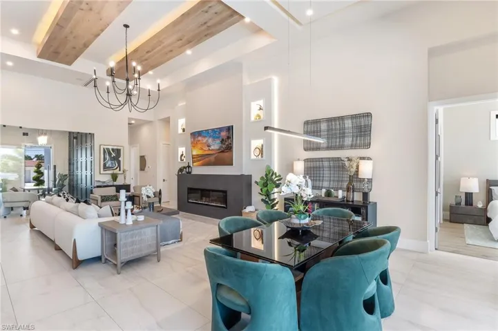 Living area with a towering ceiling, a chandelier, recessed lighting, a glass covered fireplace, and beam ceiling