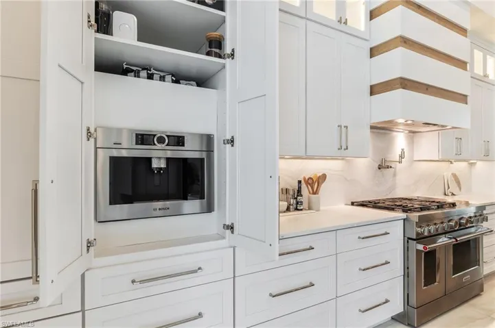 Kitchen with range with two ovens, white cabinetry, custom exhaust hood, and glass insert cabinets