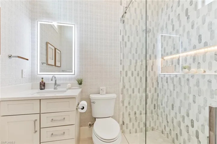 Bathroom with toilet, vanity, tiled shower, and tile walls
