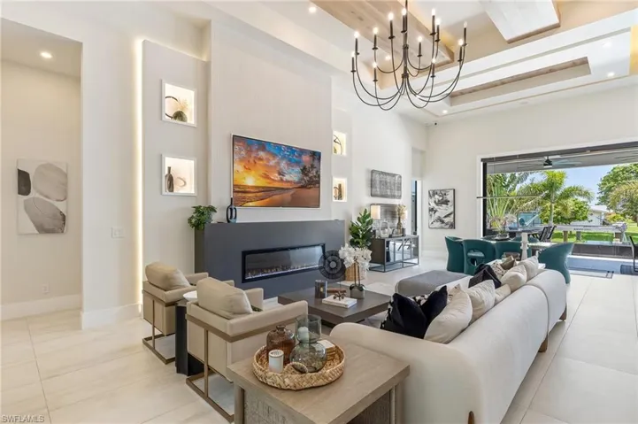 Tiled living room with a towering ceiling, a glass covered fireplace, recessed lighting, baseboards, and a tray ceiling