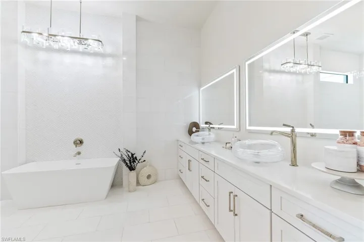 Full bath featuring double vanity, a freestanding bath, tile patterned flooring, tiled shower, and a chandelier