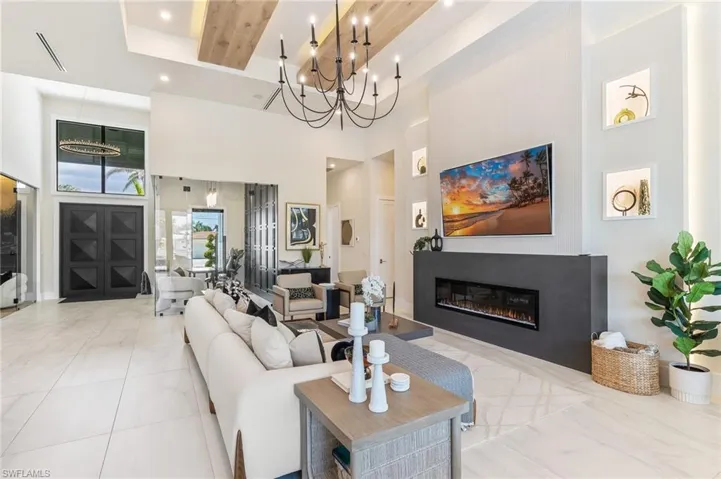 Living room with a high ceiling, a glass covered fireplace, beam ceiling, and recessed lighting