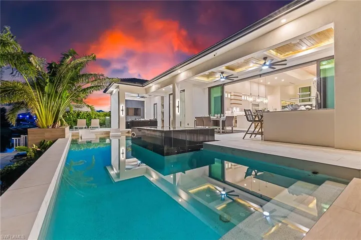Pool at dusk featuring a ceiling fan, a patio area, an outdoor pool, and exterior bar