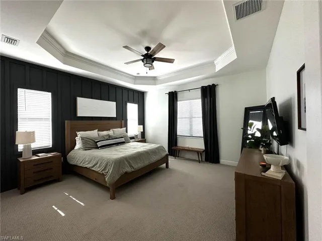 Carpeted bedroom with ceiling fan, ornamental molding, a raised ceiling, and multiple windows