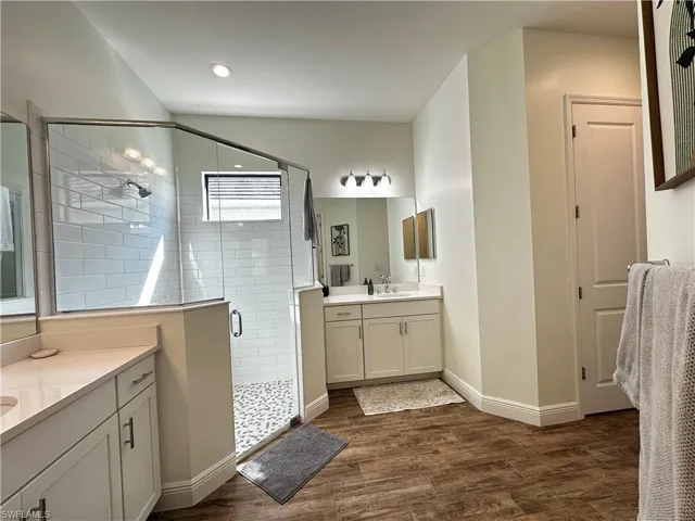 Bathroom featuring baseboards, two vanities, wood finished floors, a shower stall, and a sink