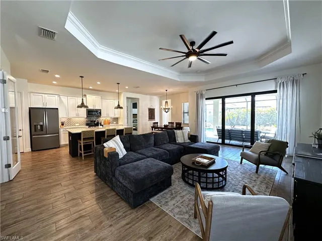 Living area featuring baseboards, visible vents, a raised ceiling, a ceiling fan, and wood tiled floor