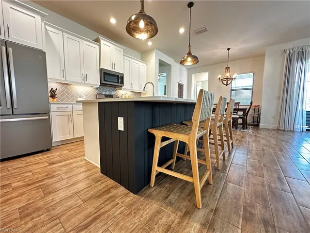 Kitchen featuring appliances with stainless steel finishes, light countertops, pendant lighting, and white cabinetry