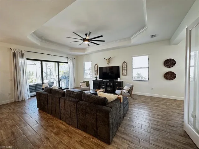 Living area featuring baseboards, visible vents, a raised ceiling, a ceiling fan, and wood tiled floor