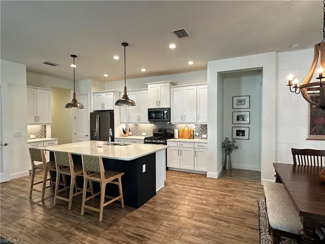 Kitchen with a sink, white cabinetry, light countertops, black appliances, and an island with sink