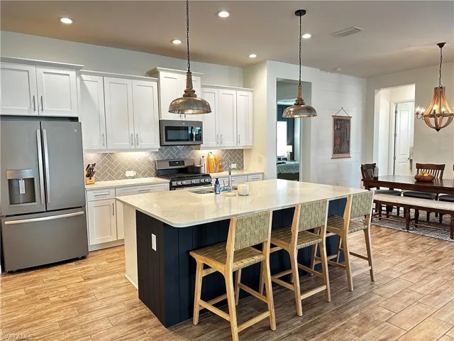 Kitchen with white cabinetry, GE Slate appliances, and a center island with sink