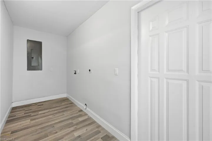 Dedicated utility area featuring wood-finish flooring, white baseboards, and a paneled door