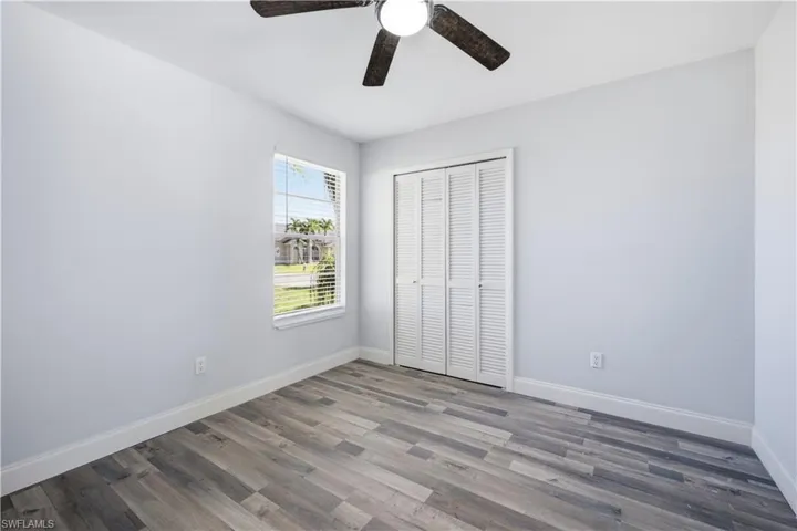 Room featuring wood-finish flooring, a window with blinds, and white louvered bifold closet doors