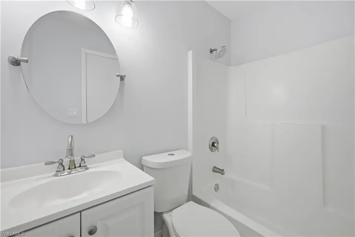 Full bathroom featuring a white vanity with integrated sink, chrome faucet, and a round wall-mounted mirror