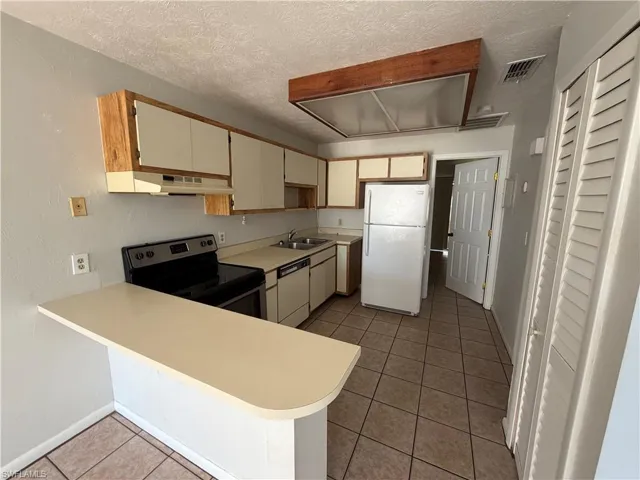 Two tone kitchen with white appliances, light countertops, a peninsula, light tile patterned floors, and a textured ceiling