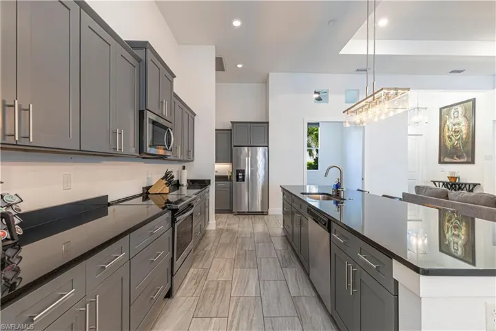 Kitchen featuring appliances with stainless steel finishes, a sink, a large island, hanging light fixtures, and gray cabinetry