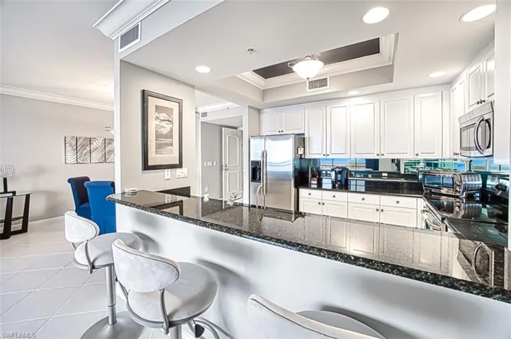 Kitchen featuring a raised ceiling, kitchen peninsula, stainless steel appliances, ornamental molding, and white cabinets