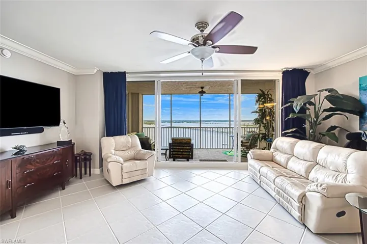 Tiled living room featuring ceiling fan, expansive windows, ornamental molding, and a water view