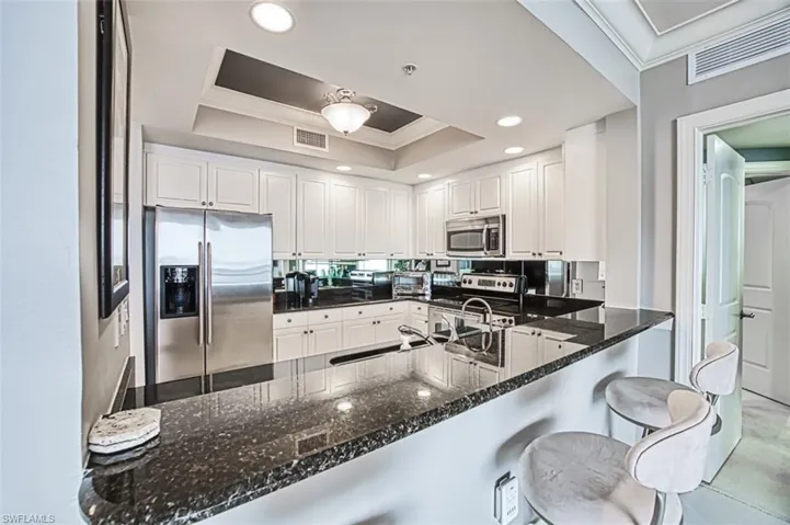 Kitchen with a tray ceiling, kitchen peninsula, white cabinets, and stainless steel appliances