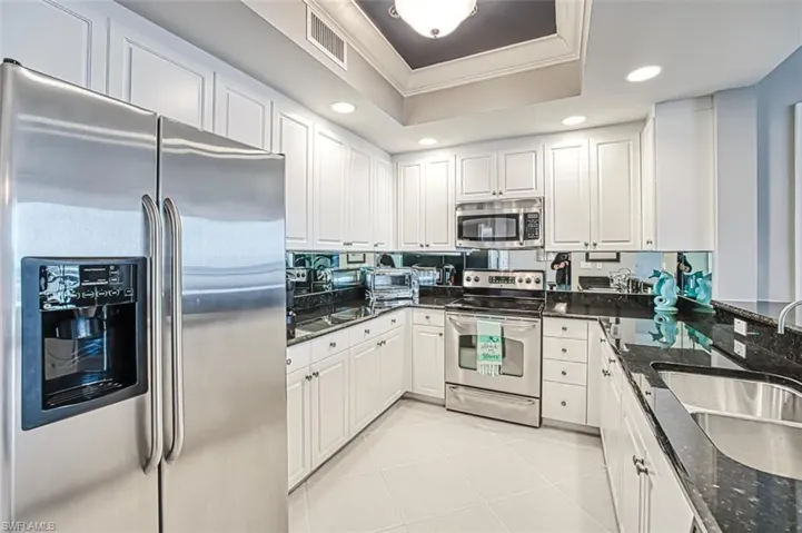 Kitchen with sink, a tray ceiling, white cabinetry, appliances with stainless steel finishes, and dark stone counters