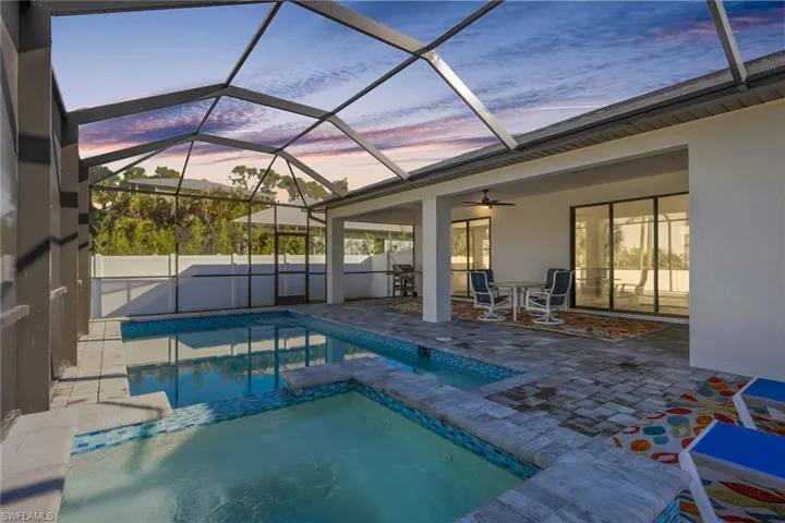 View of swimming pool featuring a sunroom, a patio area, glass enclosure, a pool with connected hot tub, and outdoor dining space