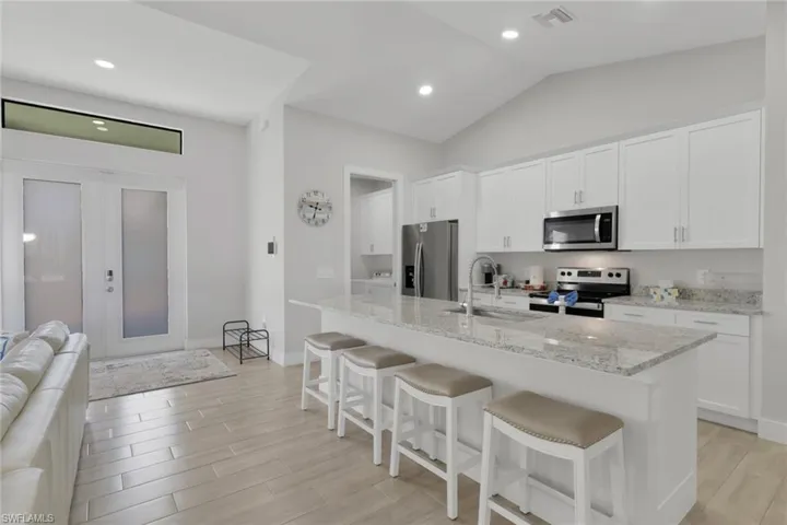 Kitchen with a kitchen breakfast bar, white cabinetry, wood tiled floors, stainless steel appliances, and lofted ceiling