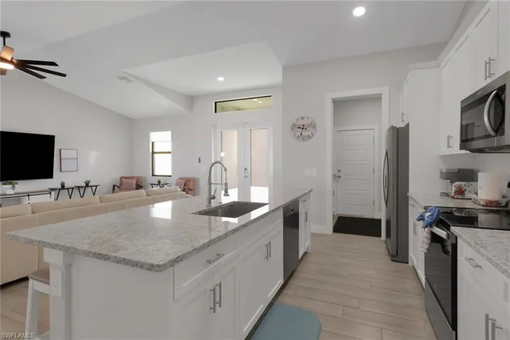 Kitchen featuring white cabinets, black appliances, open floor plan, light stone countertops, and recessed lighting