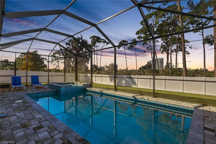 View of swimming pool featuring glass enclosure, a sunroom, a pool with connected hot tub, and a patio