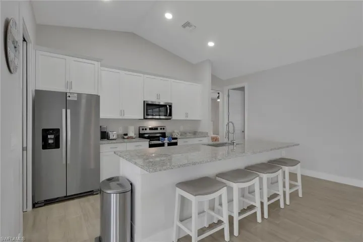 Kitchen featuring stainless steel appliances, white cabinetry, light stone counters, vaulted ceiling, and a kitchen breakfast bar