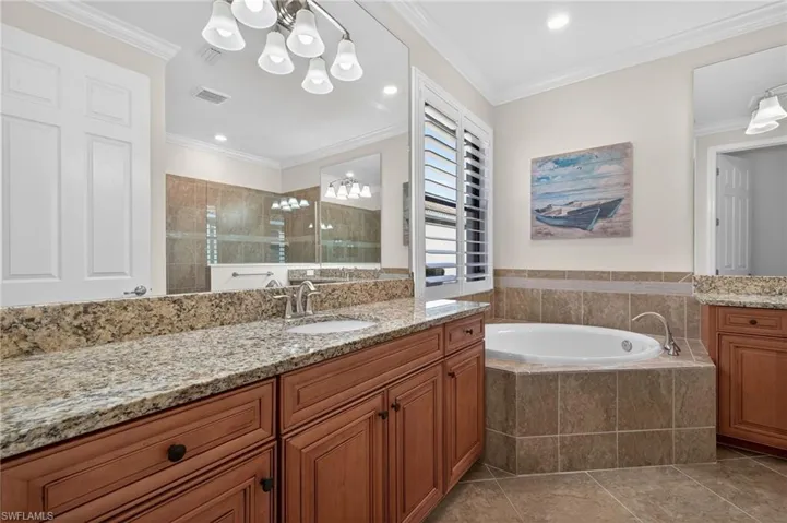 Bathroom with two vanities, a tile shower, a garden tub, crown molding, and light tile patterned floors